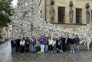 Eine Gruppe von Jugendlichen steht vor dem Kunstwerk "Forx", das aus weißgestrichenen Heugabeln besteht, die Bretter auf den Zinken haben.