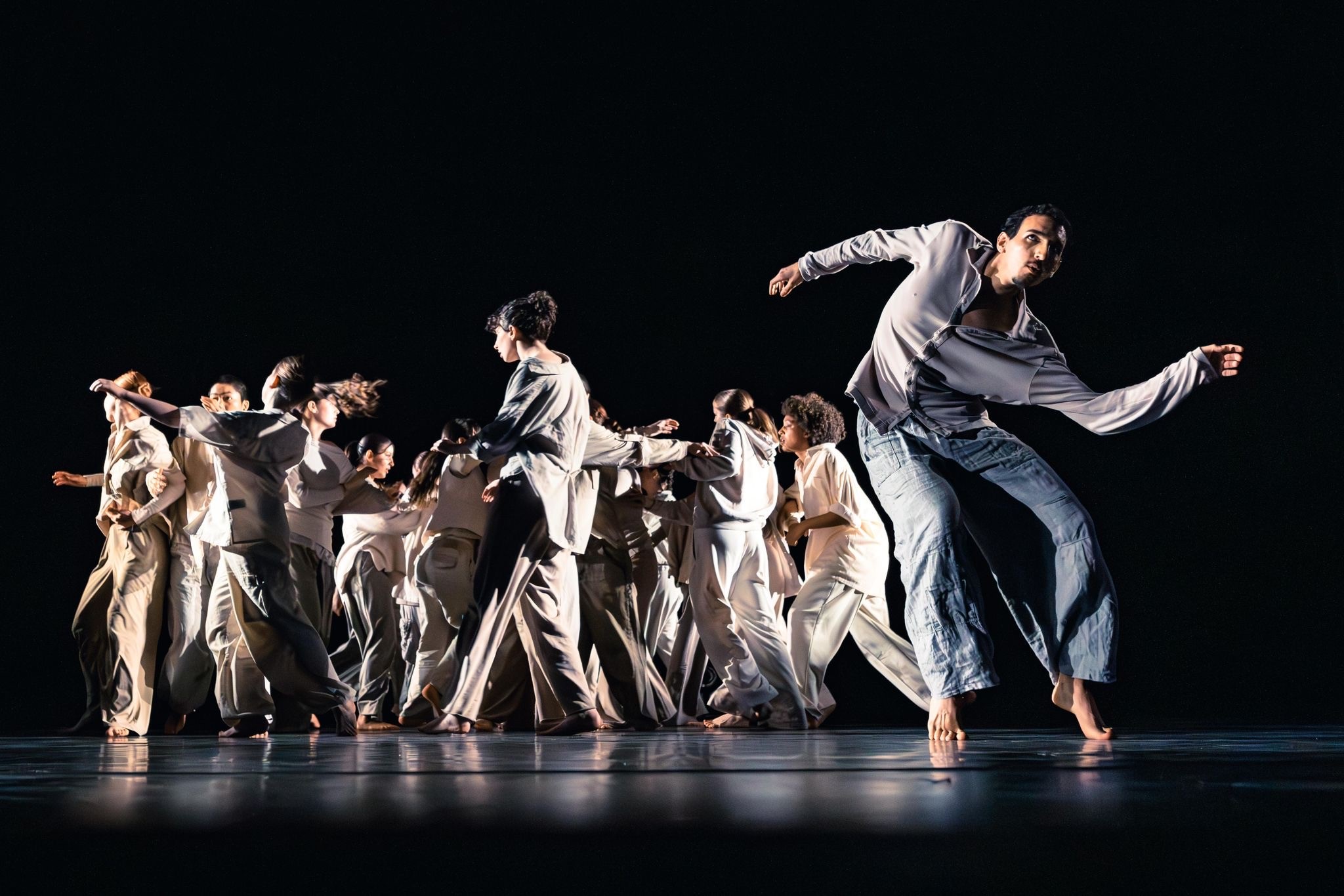 ein Tänzer in heller Kleidung bewegt sich vor einer Gruppe weiterer Tänzer