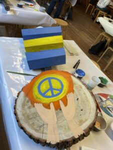 Baumscheibe, bemalt: Zwei Hände halten ein Peace-Zeichen in die Höhe