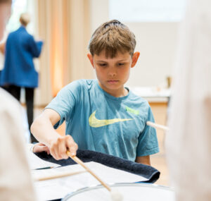 Junge im blauen T-Shirt an kleiner Trommel