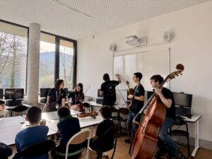 Musiker mit Streichinstrumenten in einem Klassenraum mit Schülern. Ein Musiker schreibt an die Tafel.