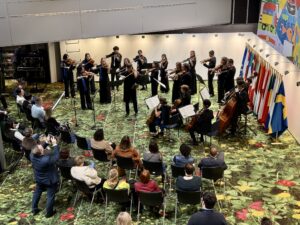 Blick von oben auf ein Kammerorchester, das in einem Foyer mit grünem Teppich spielt.