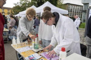 3 junge Männer in Laborkitteln neigen sich über ein chemisches Experiment.