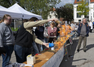 langer Tisch, im Vordergrund ein Experiment mit orangener Flamme.
